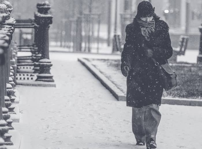 Fraun geht bei Schneefall, dick eingepackt einen Gehweg entlang