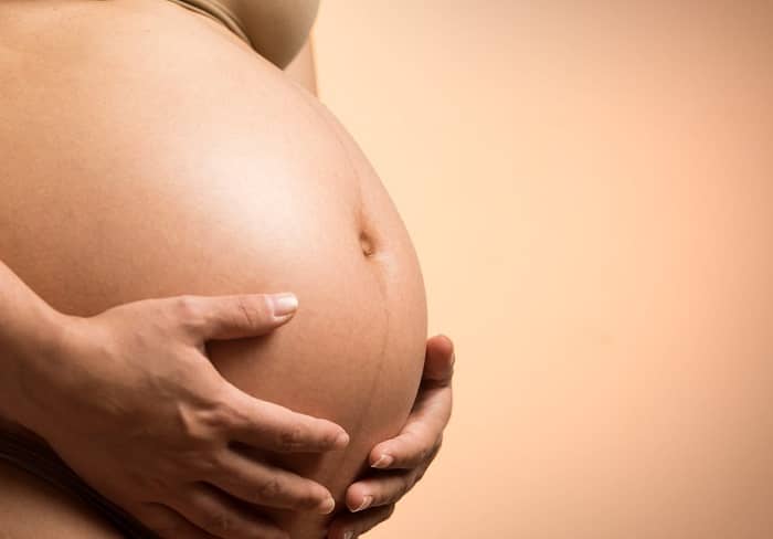 Ein Schwangerschaftsbauch wird von den beiden Händen der Schwangeren gehalten