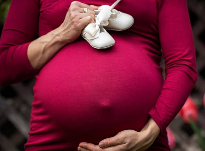 Eine schwangere Frau hält zwei Baby Schüchien in der Hand