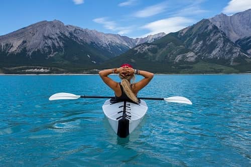 Eine Frau sitzt entspannt in einem Kajak, mitten auf einem See vor einer Bergkulisse