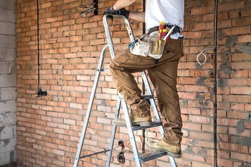 Ein Elektriker steht auf einer Leiter und verlegt Elektroleitungen