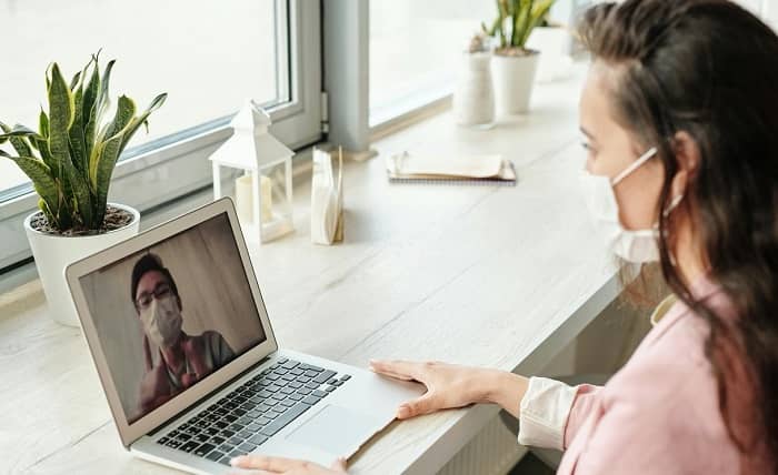 Zwei Personen mit Hygiene Gesichtsmasken unterhalten sich am Laptop